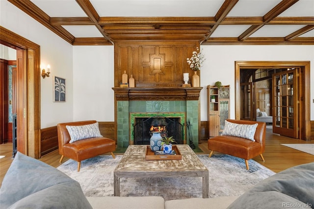 living room featuring coffered ceiling, hardwood / wood-style floors, a tiled fireplace, and beamed ceiling