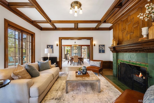 living room featuring a tile fireplace, an inviting chandelier, hardwood / wood-style floors, radiator heating unit, and coffered ceiling