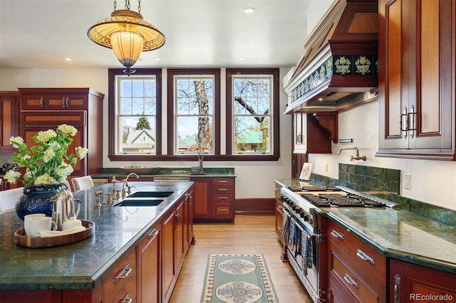 kitchen featuring sink, dark stone countertops, hanging light fixtures, high end stainless steel range, and light wood-type flooring