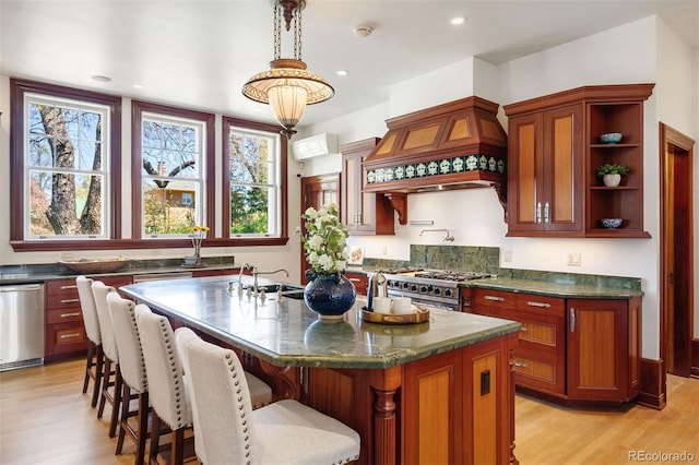 kitchen with sink, decorative light fixtures, an island with sink, custom range hood, and stainless steel appliances