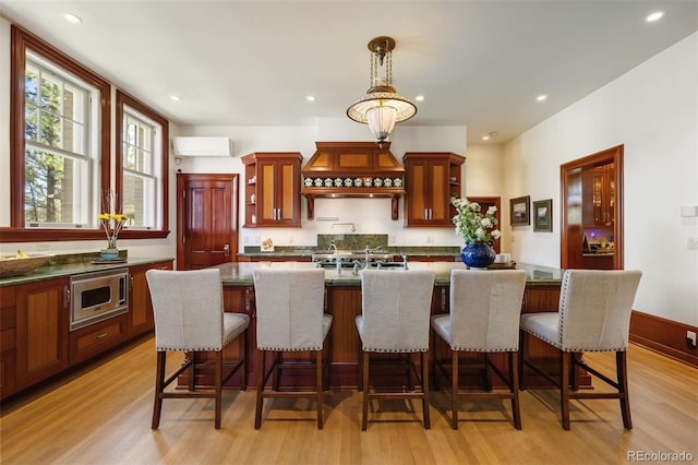 kitchen with premium range hood, pendant lighting, stainless steel microwave, a kitchen bar, and light hardwood / wood-style flooring