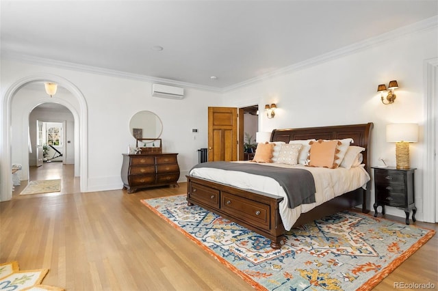 bedroom with crown molding, a wall unit AC, and light hardwood / wood-style floors