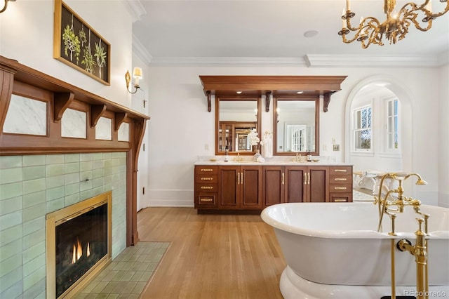 bathroom with ornamental molding, a bath, vanity, a tiled fireplace, and hardwood / wood-style floors