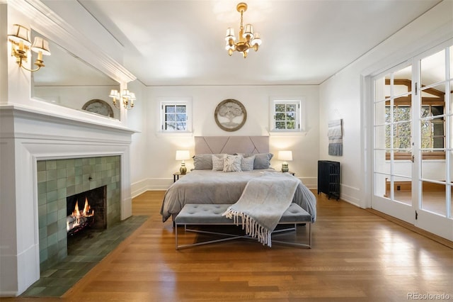 bedroom with hardwood / wood-style floors, a tile fireplace, and a notable chandelier