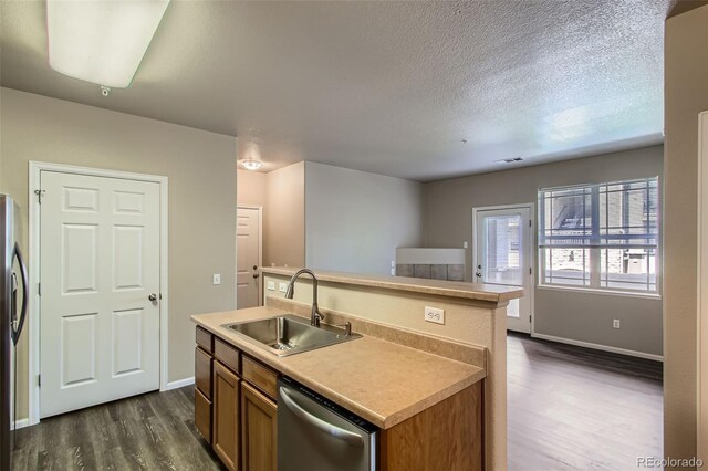kitchen with dark wood-style flooring, a center island with sink, dishwasher, a sink, and baseboards