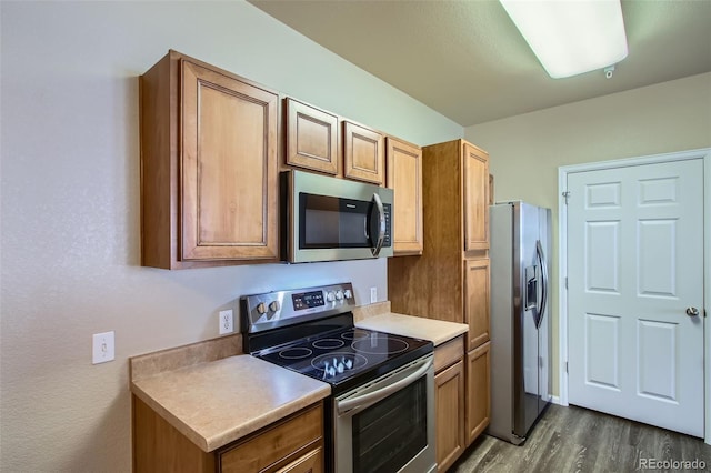 kitchen featuring light countertops, appliances with stainless steel finishes, brown cabinetry, and dark wood-style flooring