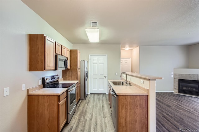 kitchen with brown cabinetry, wood finished floors, a sink, light countertops, and stainless steel appliances