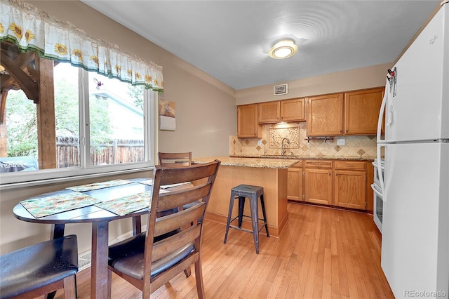 3451 Highland Pl, Westminster, CO 80031 - kitchen with a breakfast bar, light wood finished floors, freestanding refrigerator, tasteful backsplash, and visible vents