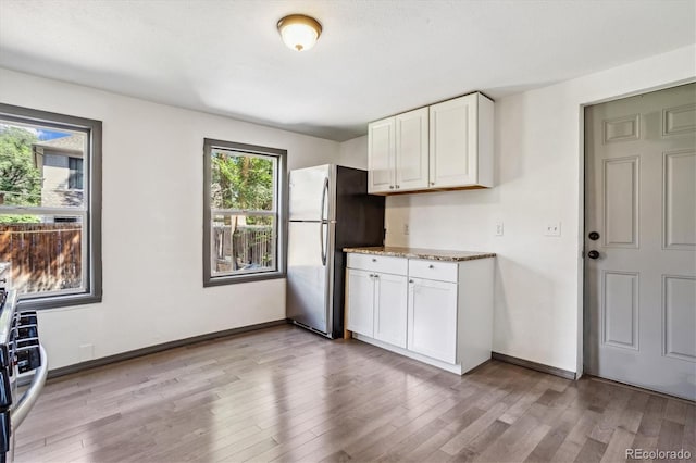 kitchen with white cabinets, stainless steel refrigerator, light hardwood / wood-style flooring, and stone counters