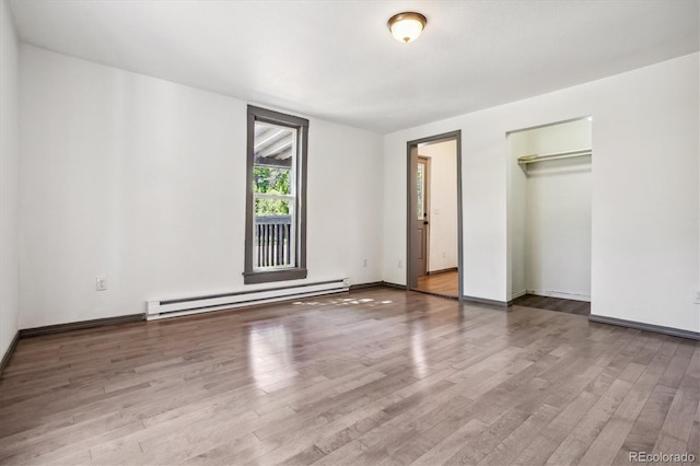 unfurnished bedroom with a walk in closet, a baseboard heating unit, hardwood / wood-style flooring, and a closet