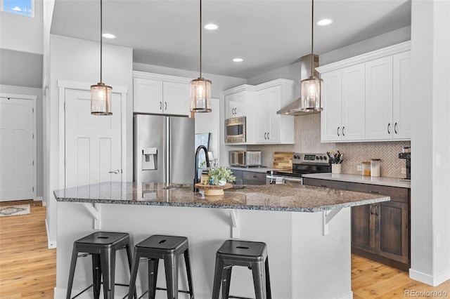 kitchen with decorative backsplash, wall chimney exhaust hood, light wood-style flooring, appliances with stainless steel finishes, and a breakfast bar