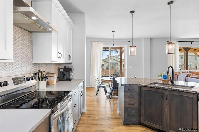 kitchen featuring stainless steel electric range oven, decorative backsplash, light wood-style floors, a sink, and wall chimney exhaust hood