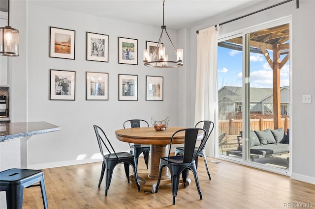 dining space featuring baseboards, light wood finished floors, and a notable chandelier