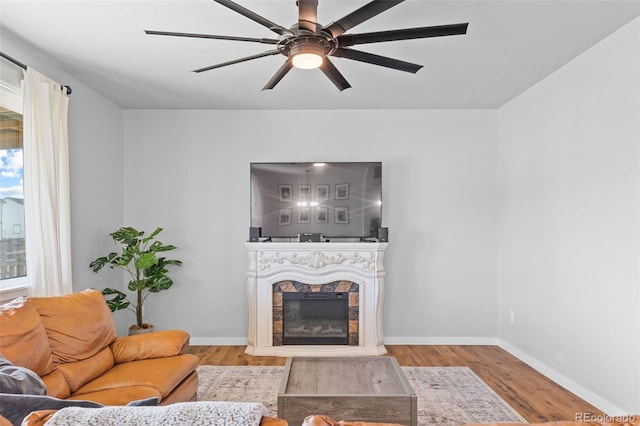 living room with ceiling fan, baseboards, wood finished floors, and a glass covered fireplace