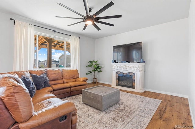 living room featuring ceiling fan, a fireplace, wood finished floors, and baseboards