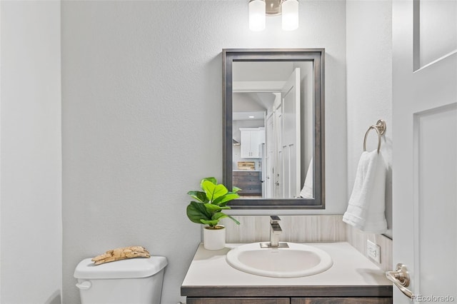 bathroom featuring a textured wall, vanity, and toilet