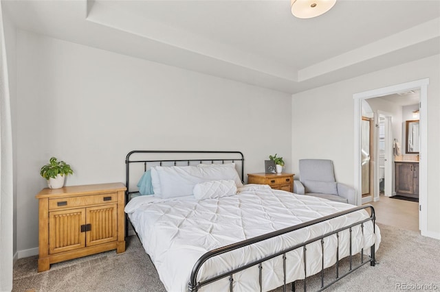 bedroom with ensuite bath, baseboards, a tray ceiling, and light colored carpet