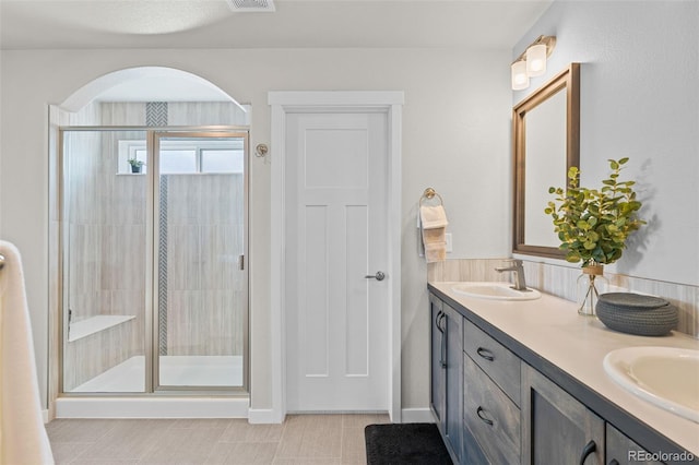 full bathroom featuring double vanity, a stall shower, and a sink