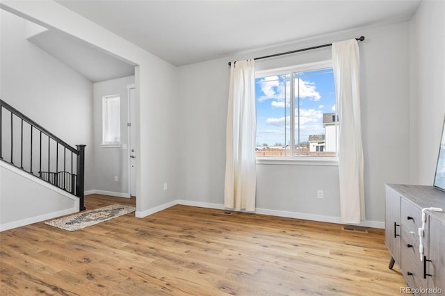 foyer featuring baseboards, visible vents, light wood finished floors, and stairs