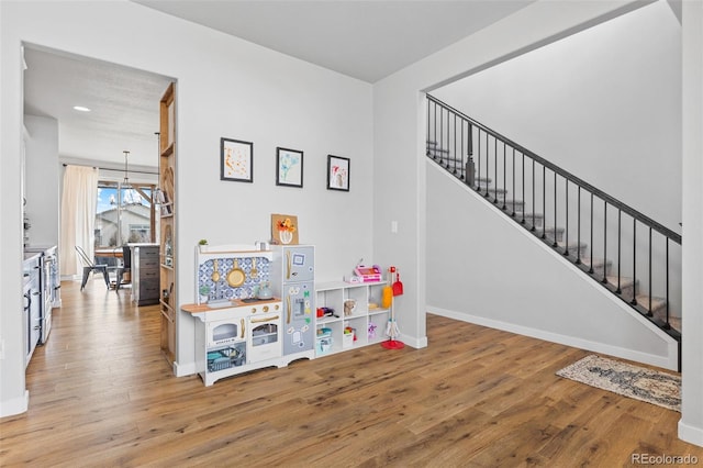 recreation room featuring baseboards, wood finished floors, and a notable chandelier