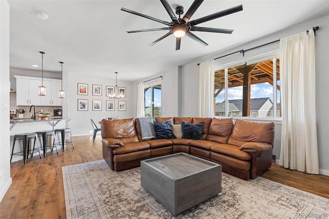 living area with light wood-type flooring, recessed lighting, baseboards, and ceiling fan with notable chandelier