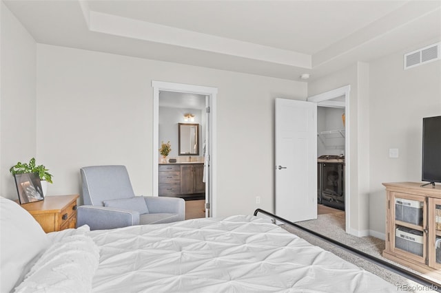 carpeted bedroom with visible vents, baseboards, connected bathroom, a tray ceiling, and a walk in closet