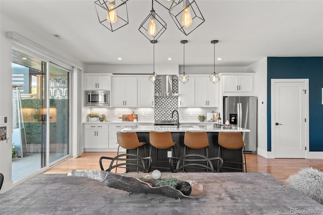 5240 N Raleigh St, Denver, CO 80212 - kitchen featuring stainless steel appliances, a breakfast bar, a center island with sink, backsplash, and white cabinets