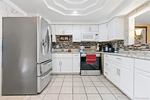 kitchen with light stone countertops, stainless steel appliances, light tile patterned floors, a tray ceiling, and white cabinetry