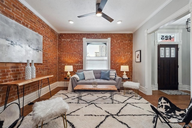 living area with plenty of natural light, brick wall, crown molding, and wood finished floors