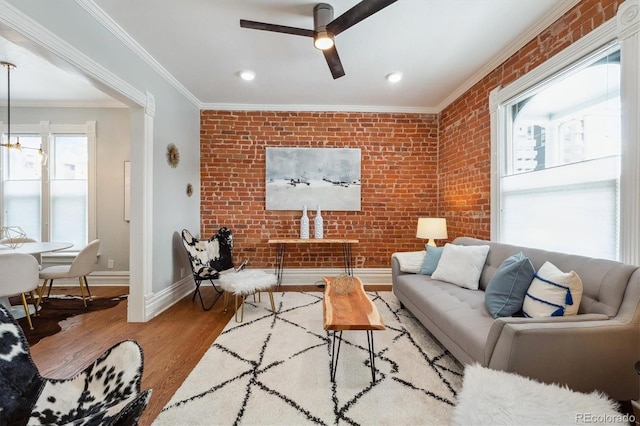 living area featuring ornamental molding, ceiling fan, brick wall, wood finished floors, and baseboards