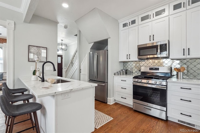 kitchen featuring a sink, white cabinetry, appliances with stainless steel finishes, a center island with sink, and glass insert cabinets