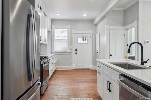 kitchen featuring light wood finished floors, white cabinets, light stone counters, appliances with stainless steel finishes, and a sink