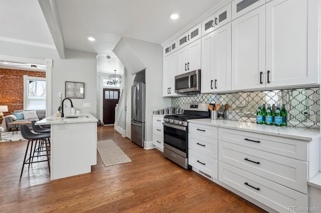 kitchen featuring appliances with stainless steel finishes, glass insert cabinets, a kitchen island with sink, a sink, and a kitchen bar