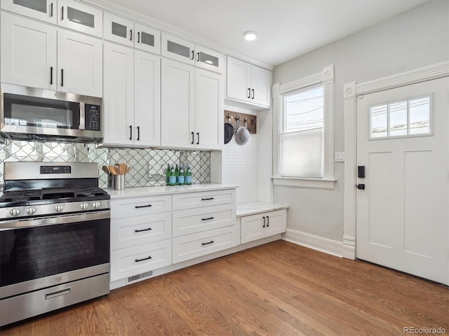 kitchen featuring backsplash, light wood-style flooring, appliances with stainless steel finishes, glass insert cabinets, and white cabinetry