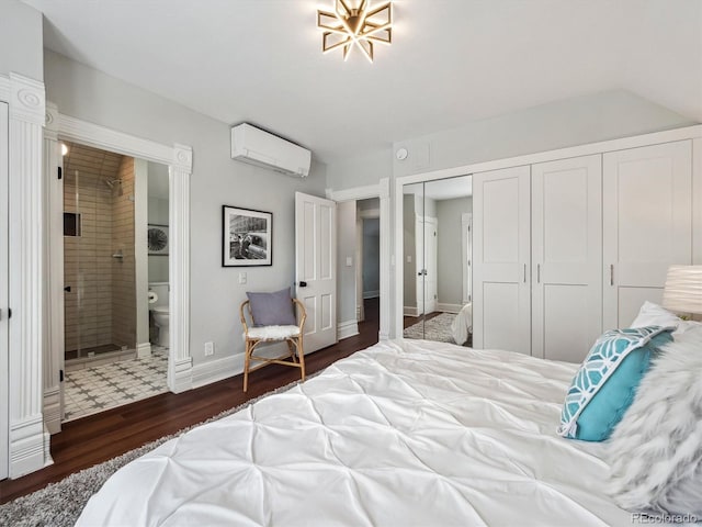 bedroom with baseboards, dark wood-style floors, ensuite bathroom, an AC wall unit, and a closet