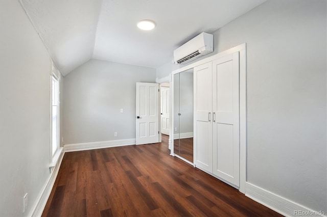 unfurnished bedroom with dark wood-type flooring, baseboards, vaulted ceiling, a closet, and a wall mounted air conditioner