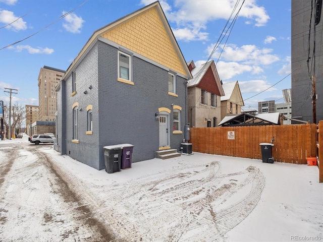 snow covered property featuring entry steps, brick siding, and fence