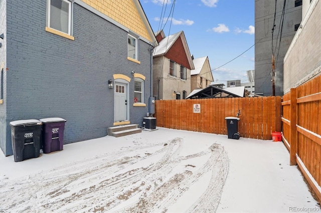 view of snowy exterior featuring brick siding and a fenced backyard