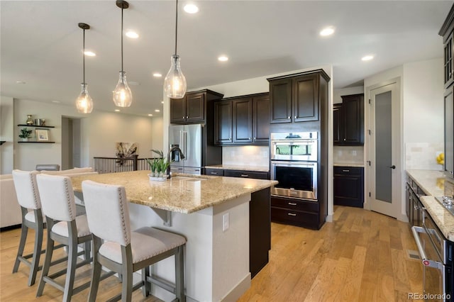 kitchen with tasteful backsplash, a sink, light wood-type flooring, and stainless steel appliances