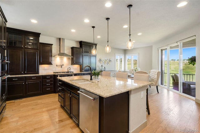 kitchen featuring a sink, wall chimney range hood, appliances with stainless steel finishes, a breakfast bar, and light stone countertops