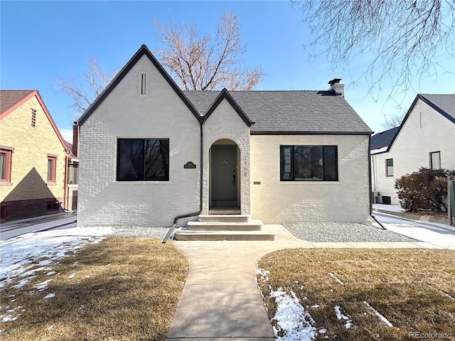 view of front facade featuring a yard, a shingled roof, a chimney, and brick siding