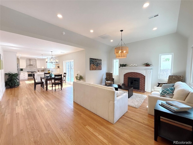 living area with a chandelier, lofted ceiling, visible vents, light wood-style floors, and a brick fireplace