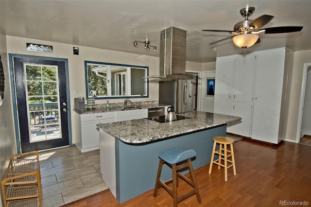 246 Baca Grant Way, Crestone, CO 81131 - kitchen featuring light wood-style flooring, island exhaust hood, white cabinetry, a kitchen breakfast bar, and appliances with stainless steel finishes