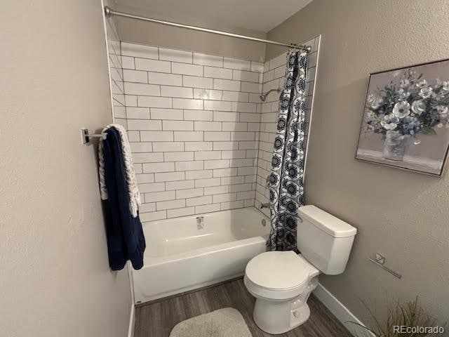 bathroom featuring toilet, shower / bathtub combination with curtain, and hardwood / wood-style flooring