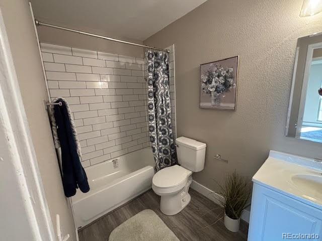 full bathroom with hardwood / wood-style flooring, toilet, shower / bathtub combination with curtain, and vanity