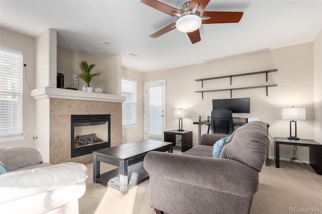 living room with ceiling fan, a tiled fireplace, and light carpet