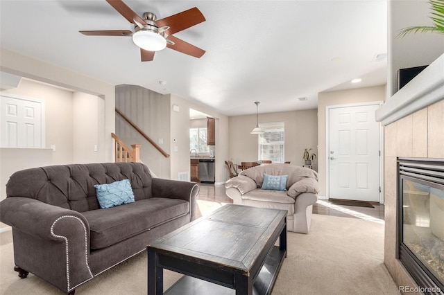 living room with ceiling fan, light colored carpet, sink, and a tile fireplace