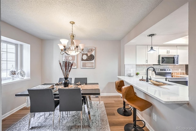 dining space with light hardwood / wood-style flooring, sink, a textured ceiling, and an inviting chandelier