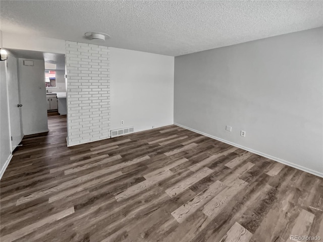 spare room with a textured ceiling, dark hardwood / wood-style flooring, and brick wall