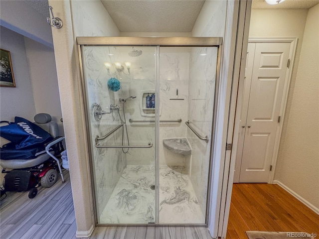 full bath with a marble finish shower, baseboards, a textured ceiling, and wood finished floors